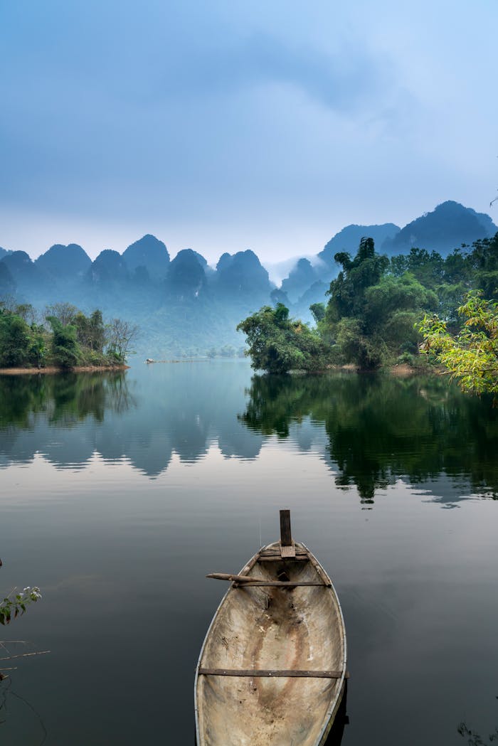 About A tranquil river scene with a canoe, misty mountains, and lush greenery, perfect for nature lovers.